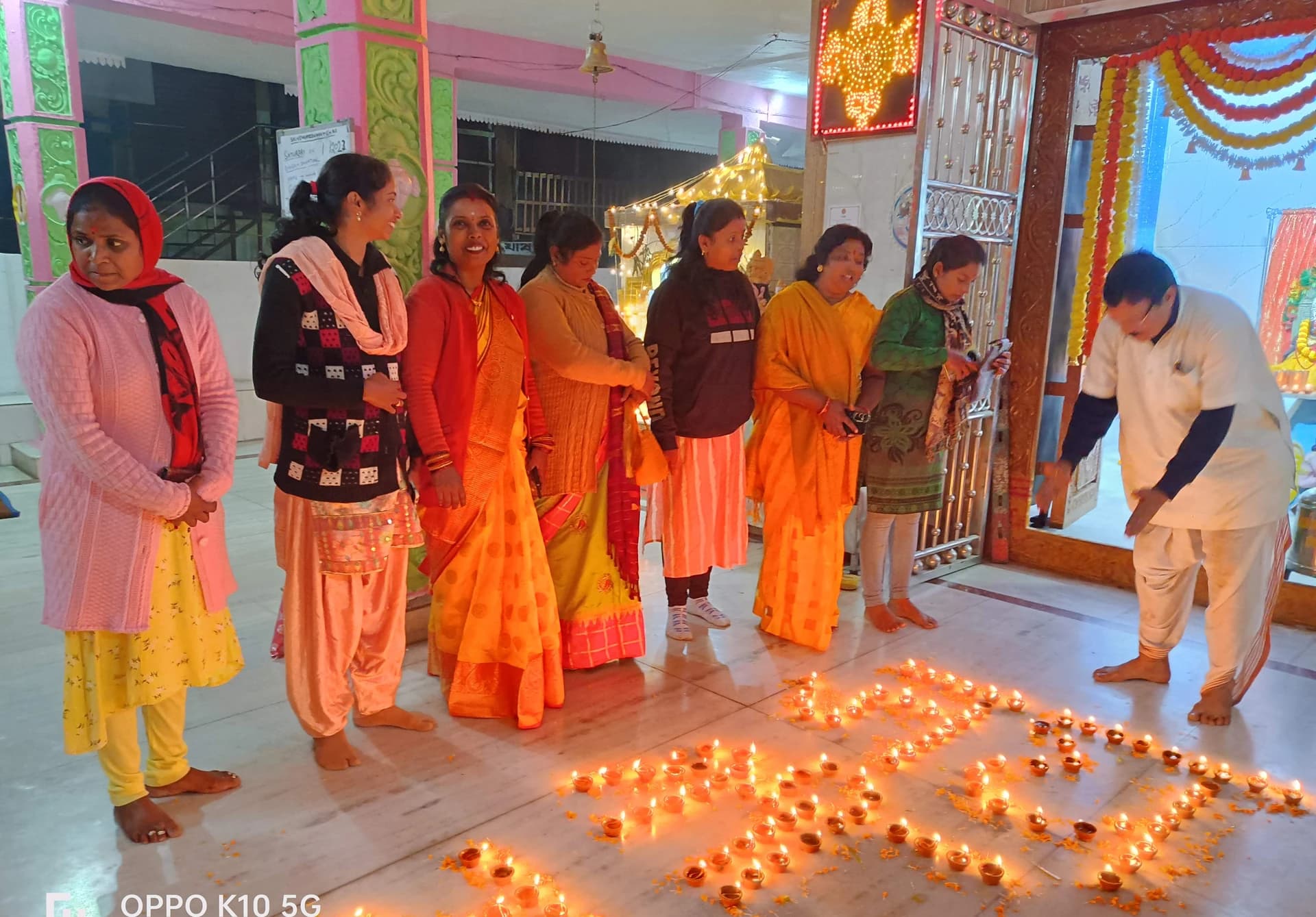 Devotees gathered for worship inside Sri Venkateswara Swamy Temple, beside oil lamps on the floor.